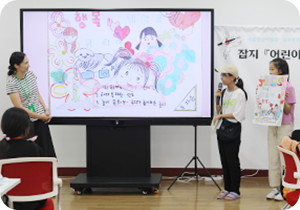 기획 전시 <어린이 나라>와 연계하여 국립한글박물관과 한국방정환재단이 공동으로 기획한 ‘잡지 『어린이』 특집호 만들기’ 현장 사진이다. 마이크를 든 한 여자 어린이가 화면을 띄워놓고 무언가를 발표하고 있다. 화면 속엔 어린이 형상의 얼굴 그림이 여러 개 그려져 있다.